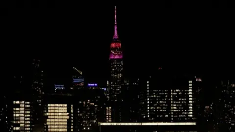 The Empire State building glows pink as part of the New York City skyline.