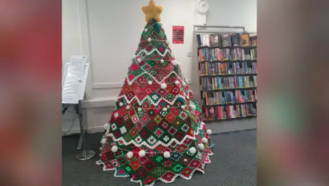 Hailsham Women's Institute a crocheted Christmas tree standing next to a bookshelf in a library