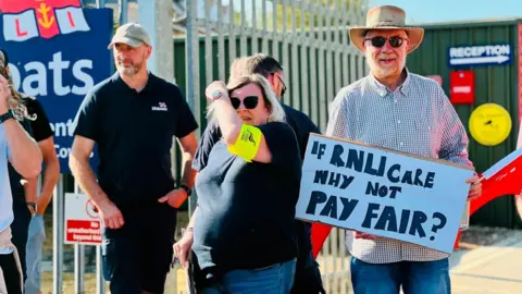 Lukas Antczak Workers on the picket line. One placard says: "If RNLI care why not pay fair?"