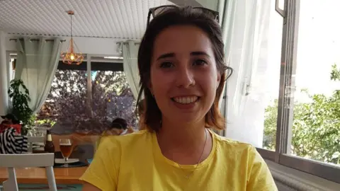 Family handout Marta Elena Vento smiles at the camera in a dining room. She has short, brown hair and wears a yellow T-shirt.