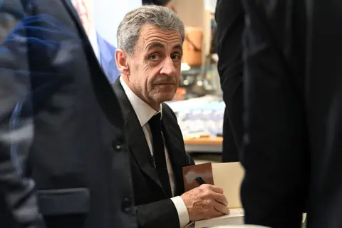 France's former President Nicolas Sarkozy looks on as he takes part in an autograph session of his book "Diary of a Prisoner" on the day of its' release at the Lamartine bookshop in Paris on December 10, 2025. Sarkozy has written a 216-page book entitled "Diary of a Prisoner," released on December 10, 2025 and excerpts of which were published in several French media on December 6, 2025. Nicolas Sarkozy, who was president from 2007 to 2012, was protected in prison by two security officers and remained confined to his cell 23 hours a day, except for visiting hours.