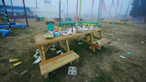 Ben Birchall/PA Media A wooden bench covered in discarded food and drink containers at Glastonbury Festival.