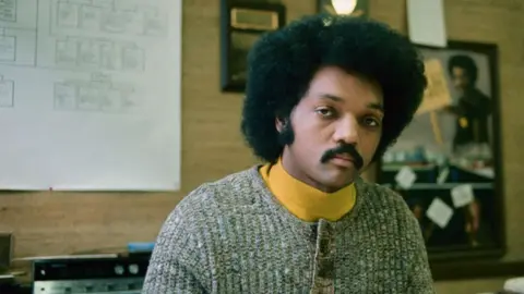 Jesse Jackson is posing at his desk with books and papers scattered around.