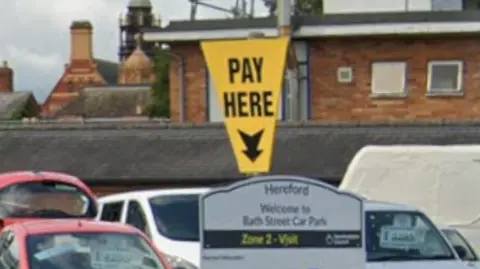 A sign saying "pay here" in a car park with an arrow pointing down