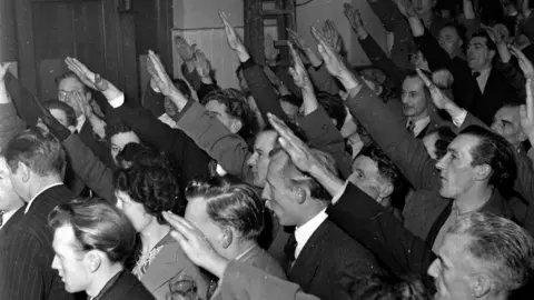 Getty Images A group of men stick their right hands in the air. 