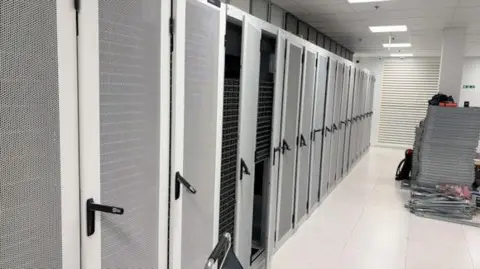 A row of locker doors at a date centre. They are predominantly grey in colour with black handles. 