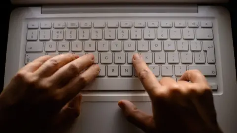 Close-up of a laptop computer keyboard, with woman's hands typing on a MacBook. Two hands are typing on the QWERTY keyboard. 