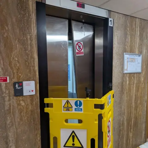Swale Borough Council A yellow barrier preventing access to a lift. One of the lift doors is at an angle, as if it has been pried open.