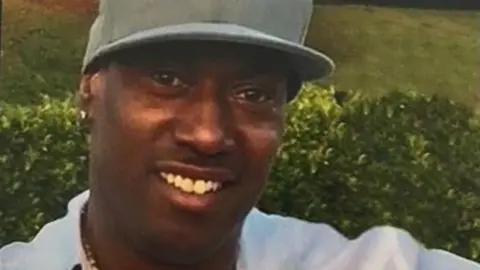 Essex Police Robert Powell appears to be taking a selfie. He is wearing a khaki-coloured baseball cap and there is greenery behind him.