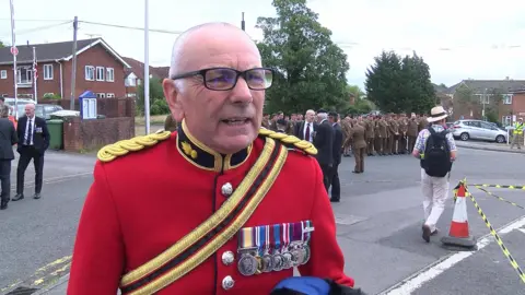 Warrant Officer Paul Thomas has short, white hair and glasses. He is wearing a military dress jacket with seven medals.