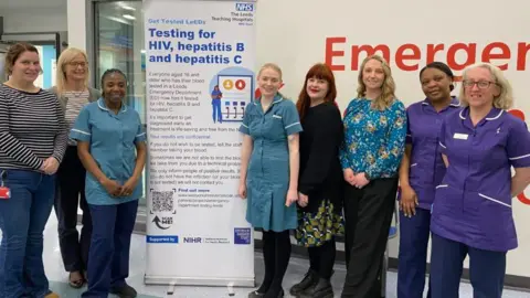 LEEDS TEACHING HOSPITALS Hospital staff standing next to a pop-up banner about testing.