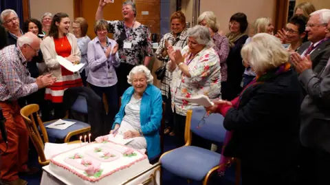 June Spencer with a birthday cake and surrounded by people 