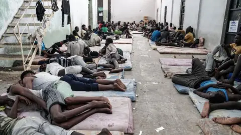 Getty Images Dozens of men sleep on mattresses on the ground in a detention centre