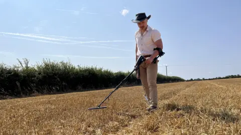 Qays Najm/BBC George Ridgway pictured using a metal detector in a field in Suffolk