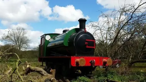 Nene Valley Railway A green steam engine with a black and red front sat on a piece of open land with a few shrubberies nearby