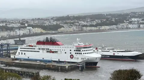 The Manxman, a large boxy ferry and the Manannan, a sleek catamaran, moored up at Douglas harbour, on a foggy day. The sea is slightly rough. 