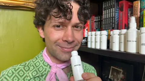 A man with curly hair wearing a green shirt and pink neck tie. 