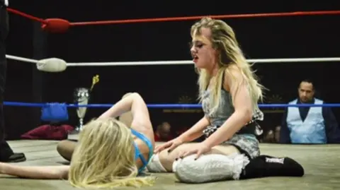 Harley Tedds/WAW Annabelle on the floor leaning over an opponent in the ring looking out of breath. 