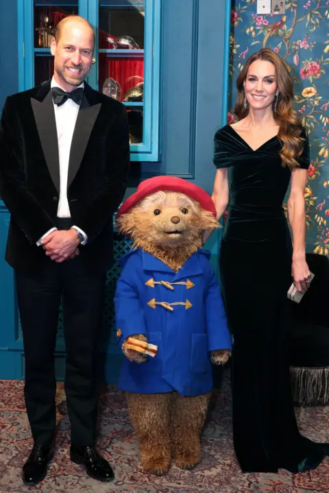 Reuters The Prince and Princess of Wales posing either side of Paddington - Catherine has her hand on the back of the bear's head 