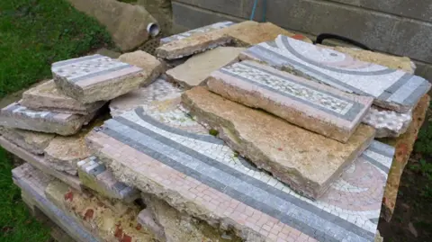 Martin Giles/BBC Lumps of broken up mosaic and concrete piled up on grass.