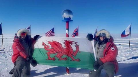 Georgina Gilbert and Rebecca Openshaw-Rowe posing with a Welsh flag at the ceremonial South Pole.