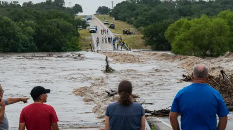 A group of people observe a flooded road