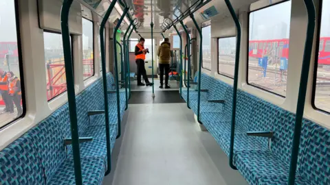 New DLR carriage shows turquoise seating and two people at far end