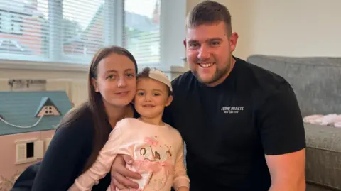 Parents Laura and Sean in a living room with their daughter Poppy in  Nottinghamshire