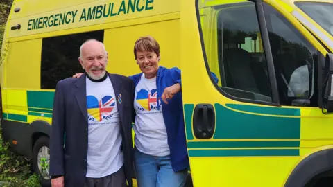 Malmesbury Town Council Two people smiling outside an ambulance. One person smiles with a Ukraine top on.