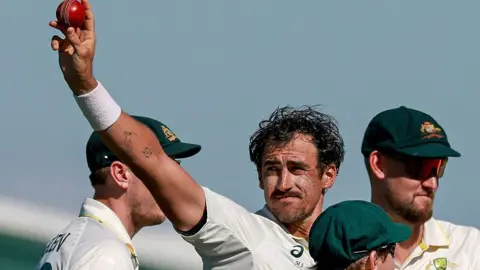Australia cricketer Mitchell Starc celebrates his 10th wicket in the match by holding the ball up