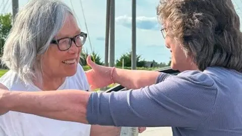 Innocence Project A smiling Sandra Hemme walks out of prison and into the arms of a female family member who is also smiling.