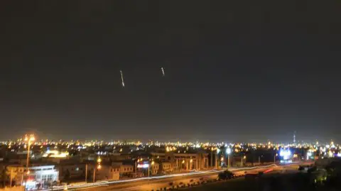 Getty Images Missiles are seen in the skies over Doha on 3 March. There are lights in the night sky and the city is lit up underneath.