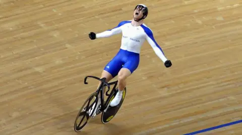 PA Chris Hoy in white and blue kit riding his bike triumphantly with his arms outstretched