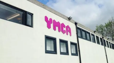 The exterior of the YMCA Sovereign Centre shows a building several windows, and trees visible nearby.
