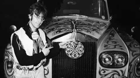 Getty Images A black and white photograph of John Lennon smiling with his psychedelic Rolls-Royce