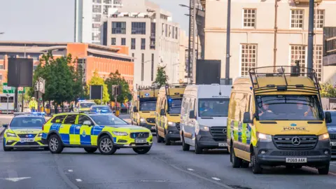 PA Media A police convoy made up of vans and cars with blue flashing lights