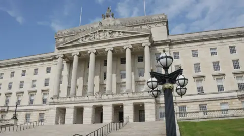 Getty Images The exterior of Stormont's Parliament Buildings. It is a four-storey, limestone building. The steps leading up the the front doors are accompanied by a long, black railing. 