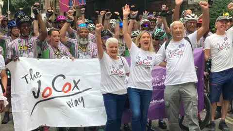 Jo's parents Jean and Gordon Leadbeater and her sister Kim with riders at The Jo Cox Way 2025 finish line