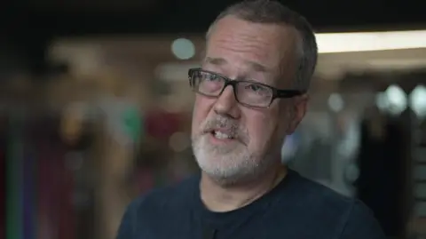 BBC Stuart Knowles, a man with a short grey beard, black glasses and short hair