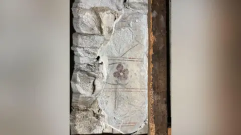 Faded painting of a red flower with a green stem on a wall. There are red lines above and below and in the middle of the flower. 