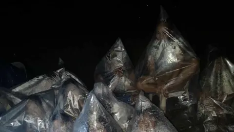 Arguel Estalicas People covered in plastic bags, which have fogged up with their breath, sitting on stools in the dark