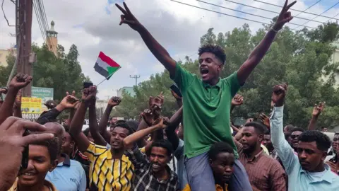 A man wearing a green shirt celebrates on the shoulders of another man