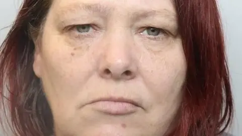 Merseyside Police A police-issued mugshot of Jayne Hill, who has long, dyed red hair and stares impassively at the camera.