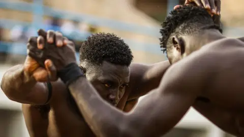 Cem Ozdel/Getty Images Two Senegalese men clasp hands as they wrestle in the capital Dakar on 9 June.