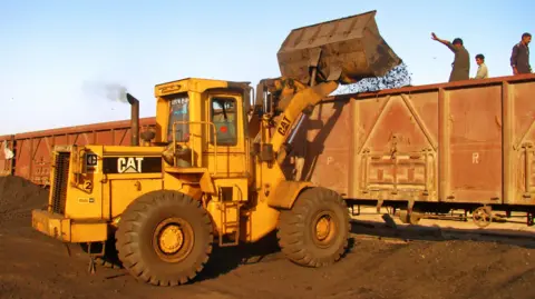 A yellow CAT digger loads coal onto a train in Pakistan.