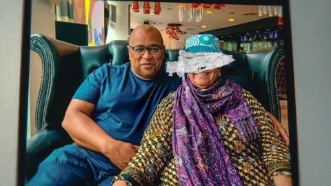 Pastry chief Graham Hornigold in a navy blue t-shirt sits with his mother Dionne Marie Hanna, wearing a baju kurung, purple scarf, teal hat, on a couch in a restaurant