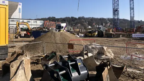 BBC/MATTHEWLOCKWOOD A close up of construction work. Two cranes are positioned on site with diggers lifting soil.