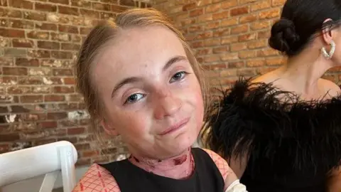 Supplied A young girl sat in a chair wearing a pink top and overalls.