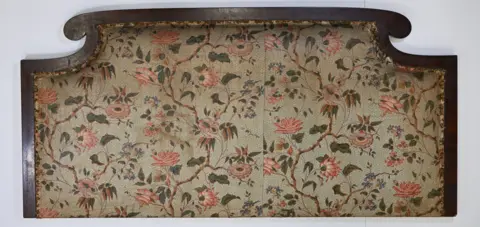 Bannockburn House Trust A headboard with a dark wooden surround and a floral print on light fabric.
