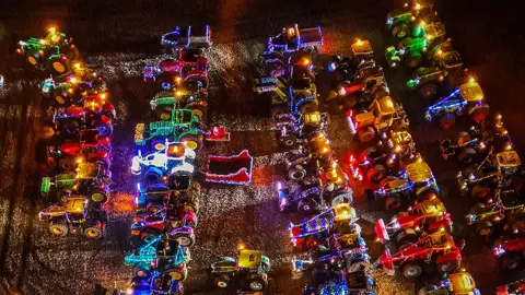 Aerial view of dozens of tractors at night illuminated with Christmas lights